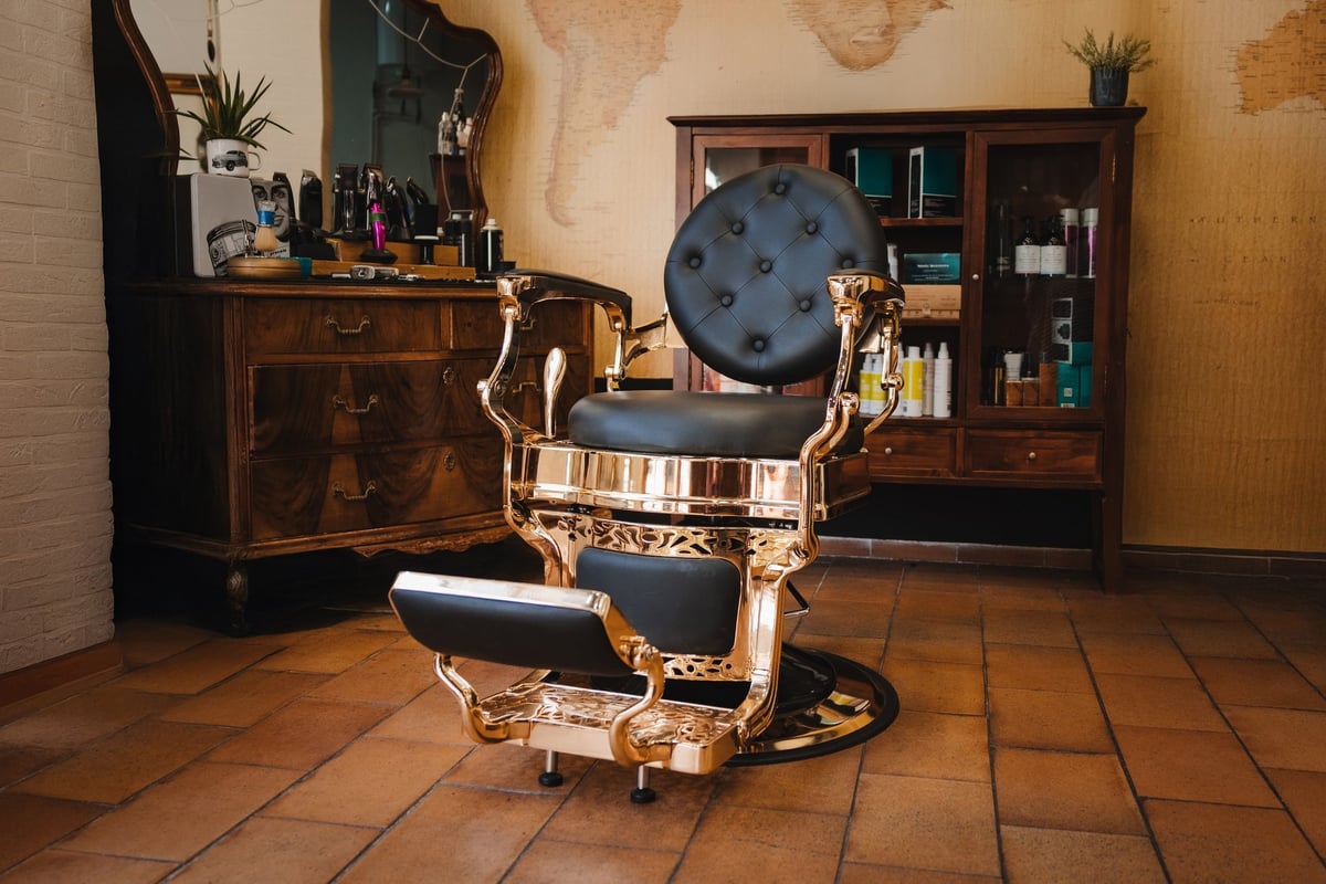 A barber shop with a gold chair and a mirror. The chair is black and has a gold trim
