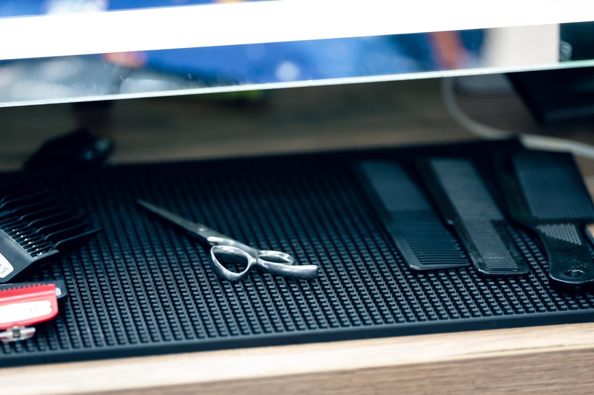 A neatly arranged set of barber tools on a workstation mat in soft indoor light